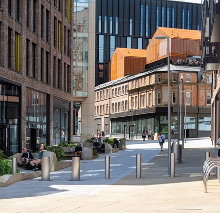 A pedestrianised shopping street in a city centre. People are strolling up and down, while others are sitting on benches.
