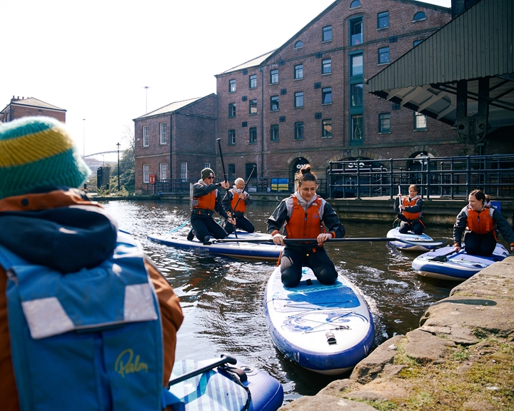 A group of people learning how to do stand-up paddle boarding at Victoria Quays in Sheffield city centre.