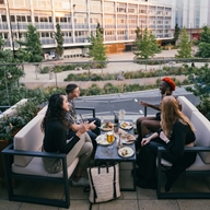 Four people are sat outside on the terrace at the restaurant The Furnace enjoying a meal.
