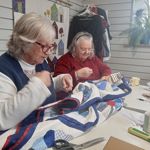 Two people sat at a table, sewing a quilt.