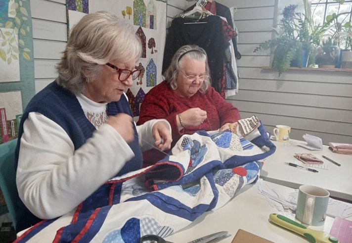 Two people sat at a table, sewing a quilt.