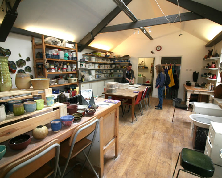 An artists studio with a huge work table and lots of shelves filled with art materials. 
