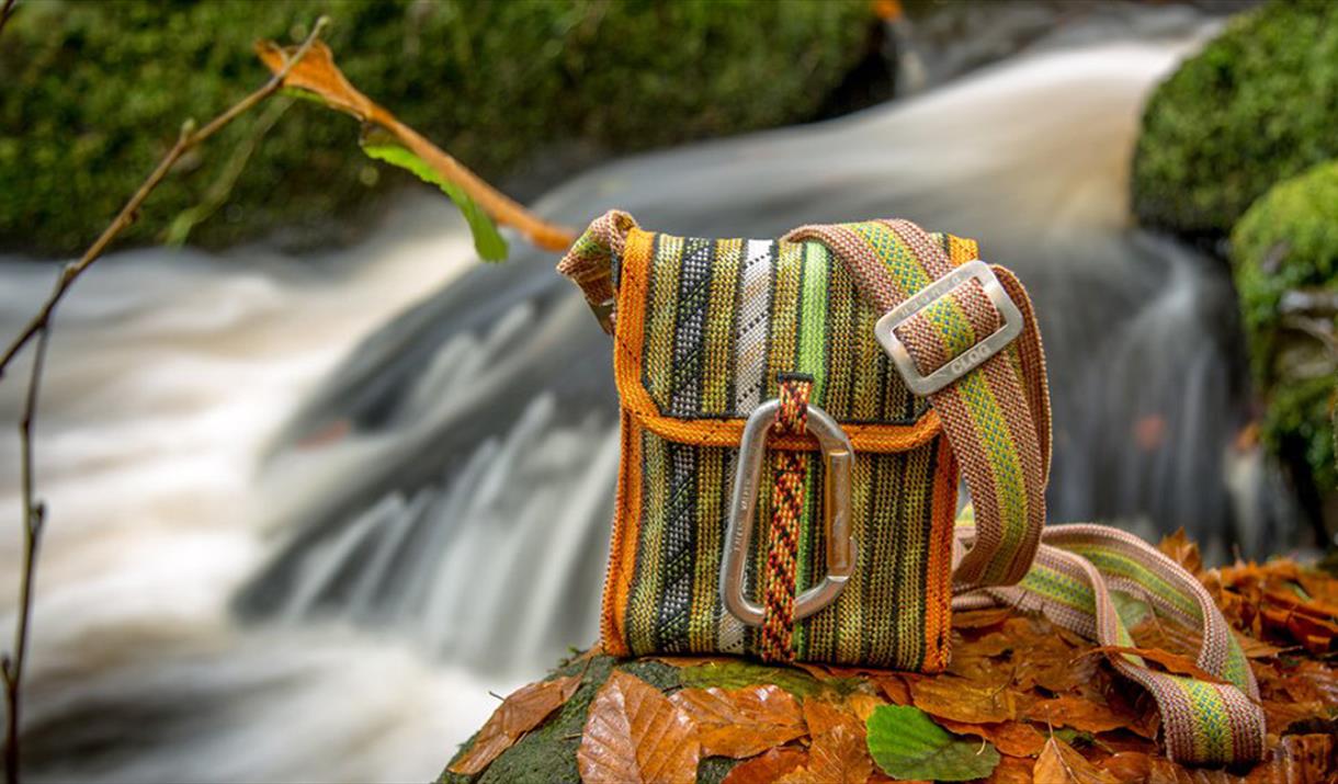 A Scavenger bag sat on a leaf-strewn rock, next to a stream.