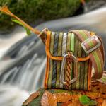 A Scavenger bag sat on a leaf-strewn rock, next to a stream.