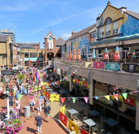 Orchard Square in the sunshine decorated with bunting. There are lots of people walking about.