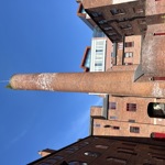 Historic brick chimney rising above a courtyard surrounded by red-brick industrial buildings under a clear blue sky.