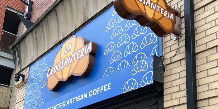 A side view of the sign outside of the shop, which reads La Croissanteria, the title is placed on top of croissant 