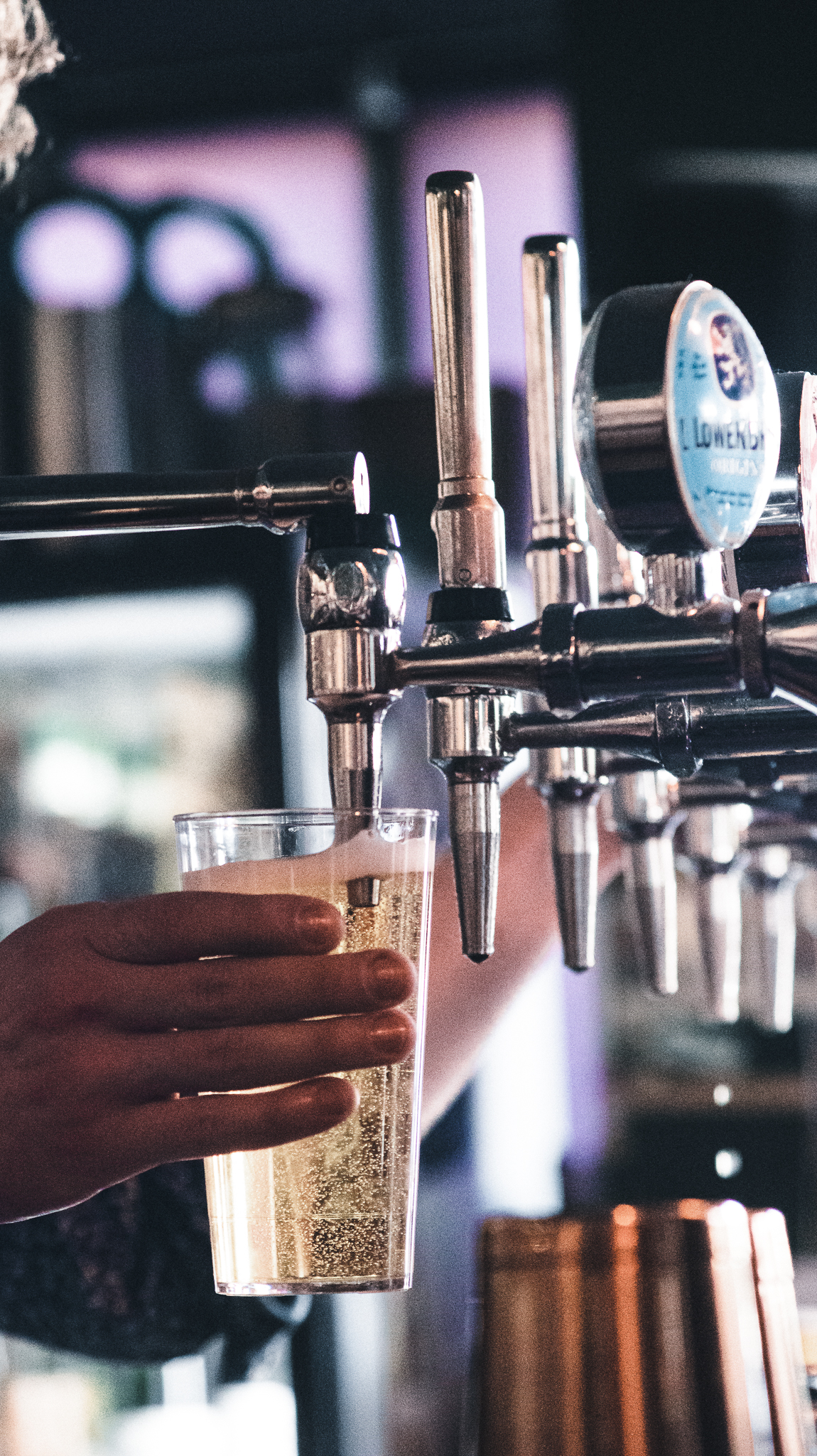 A close-up of a hand holding a plastic cup under a beer tap as a light, bubbly drink is poured.