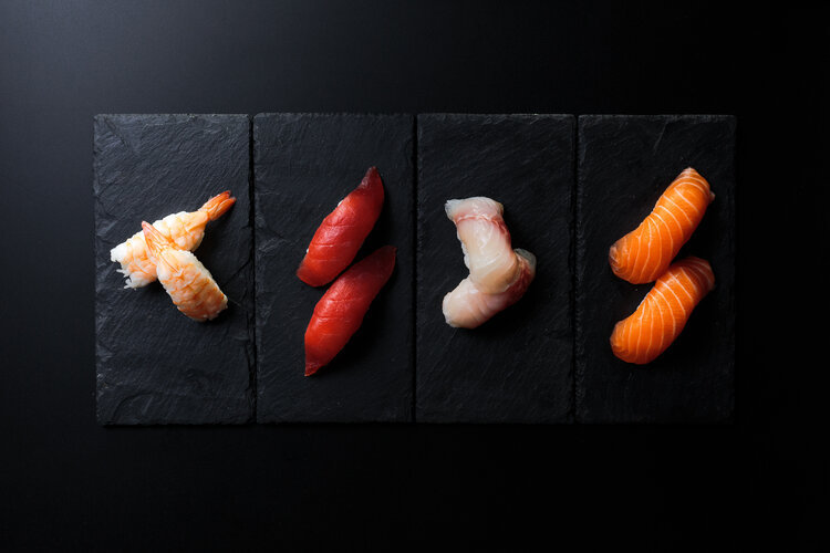 An overhead shot of four portions on sushi artfully arranged on pieces of slate.