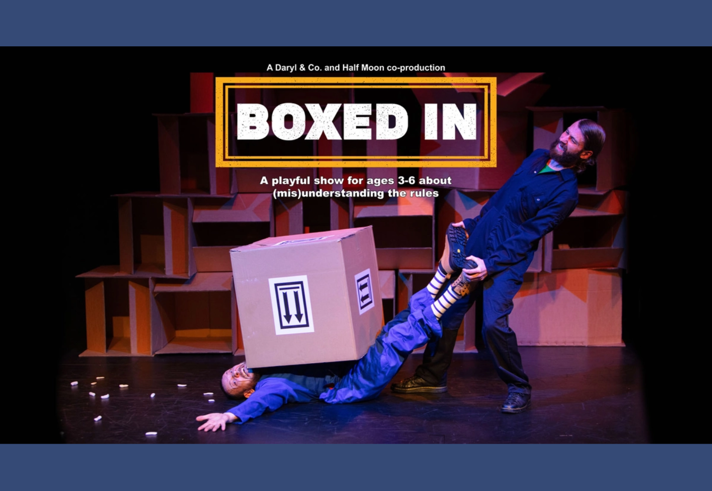 In a comedic fashion, one person is trying to pull another person out from under a huge box where they are trapped.