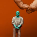 Promotional image for Woodhill featuring a small green figurine of a a man in brown clothes and handcuffs. A hand can be seen floating above the figure ready to flick it.