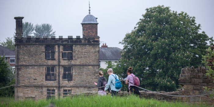 Three people with rucksacks are walking towards Sheffield Manor Lodge.