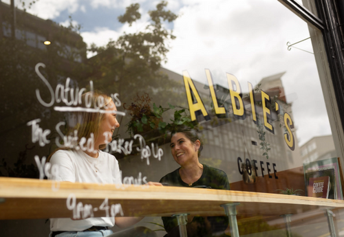 Two people sat in the window, drinking coffee, at Albie's Coffee.