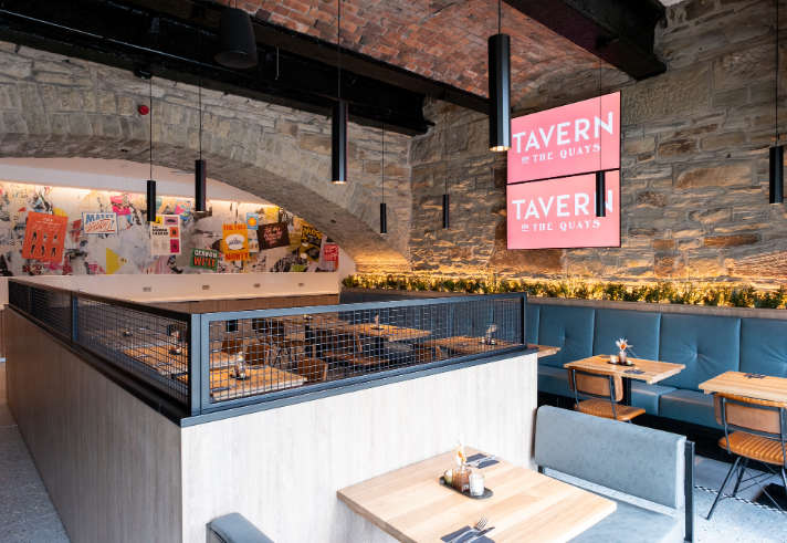 The interior of Tavern on The Quays, with bare stone walls and rows of tables and chairs.