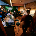 Interior shot of Public, a cocktail bar in the centre of Sheffield. There are people sat in booths and at the bar, where a barman is serving drinks.