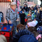 A flea circus themed magician dressed in pinstripe suit and tombola hat entertains a group of children with magic tricks