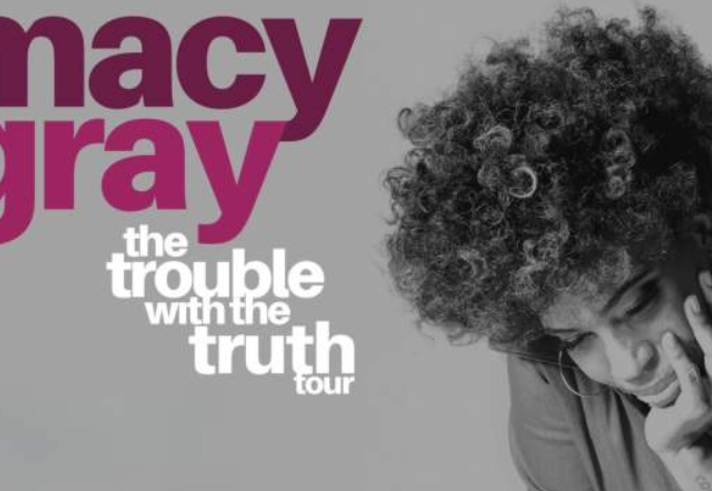 Promotional graphic for Macy Gray’s “The Trouble With The Truth Tour”. Large pink text reading “macy gray” appears on a light grey background, with the tour title in white beneath. On the right, a black-and-white portrait shows Macy Gray leaning on one hand with curly hair, filling the right side of the image. The design is simple and monochrome, with the artist’s name highlighted in bold colour.