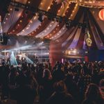 A concert taking place inside a large circus-style tent.