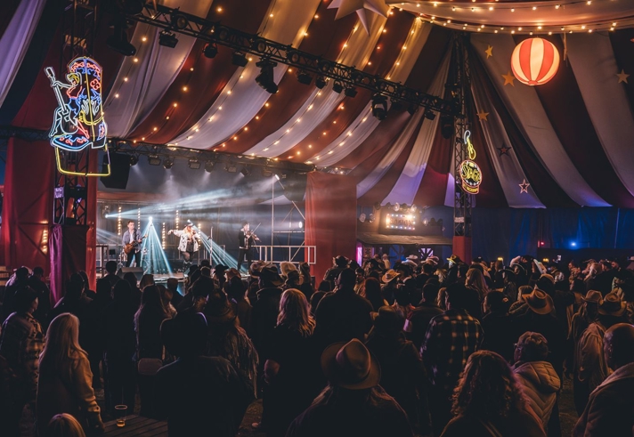 A concert taking place inside a large circus-style tent.
