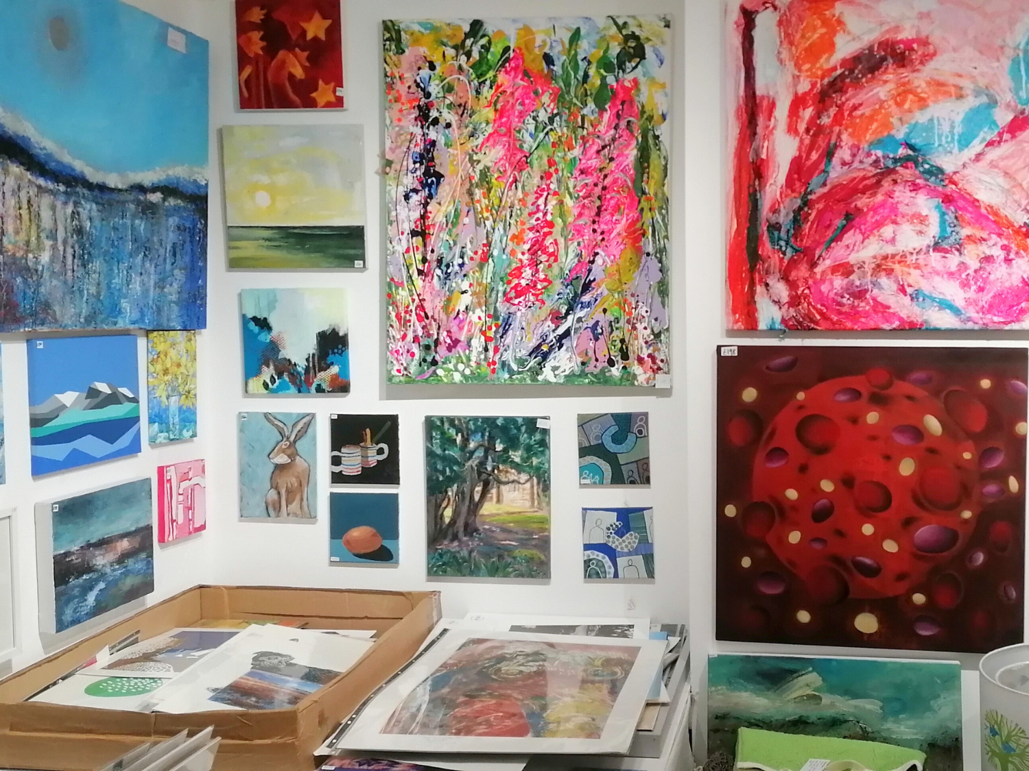 A gallery wall covered in paintings and artworks of all sizes. There are also tables covered in more paintings.