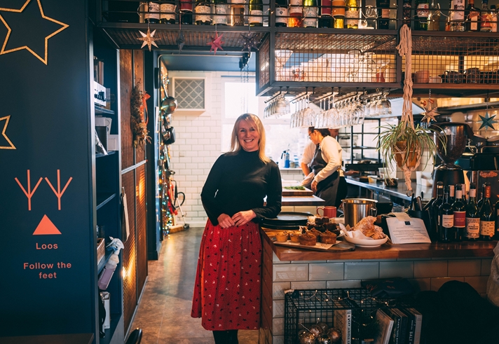 A woman stands smiling in a restaurant kitchen.