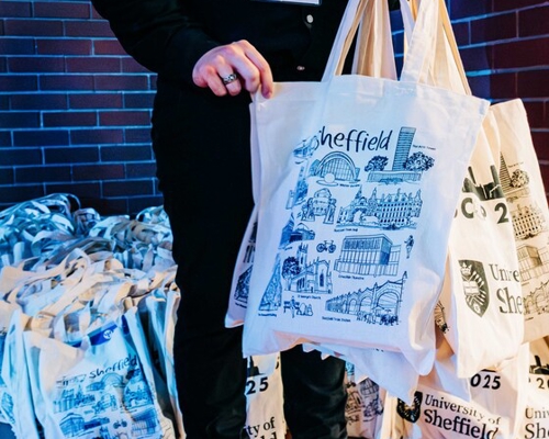 People standing around a long table covered with rows of name badges, selecting or searching for their badges in a modern event registration area.