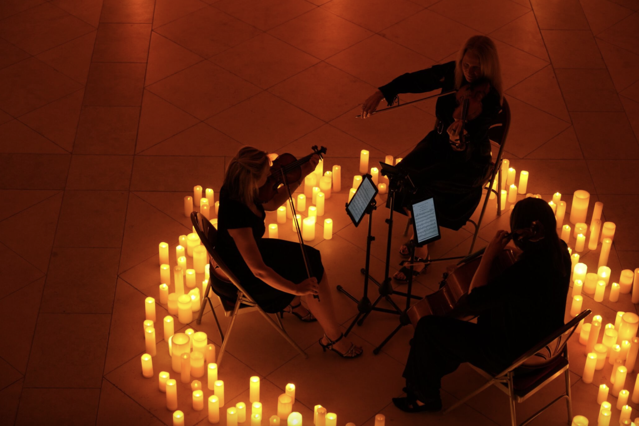 A string trio sit playing, facing each other inside a circle of lots of candles.