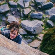 A woman climbing up a rock face as seen from above. She is clearly having fun and is determined to reach the top.