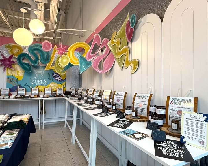 Display table inside the pop-up market showcasing rows of jars and informational cards about products, with colorful signage and decorative wall art in the background