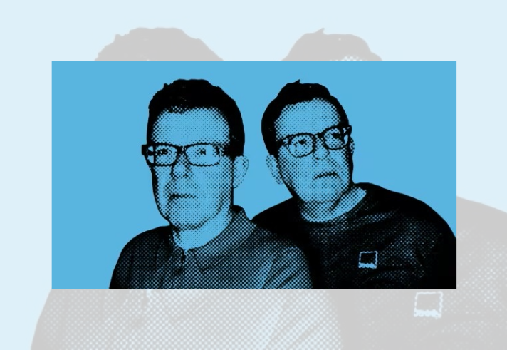 Stylised two-colour graphic portrait of two people wearing glasses, shown from the shoulders up against a light blue background. The image uses a halftone printing effect with black and blue tones, creating a retro pop-art appearance. One person faces slightly left in the foreground while the other stands behind, looking to the side. The design has a bold, poster-like aesthetic with high contrast and simplified details.