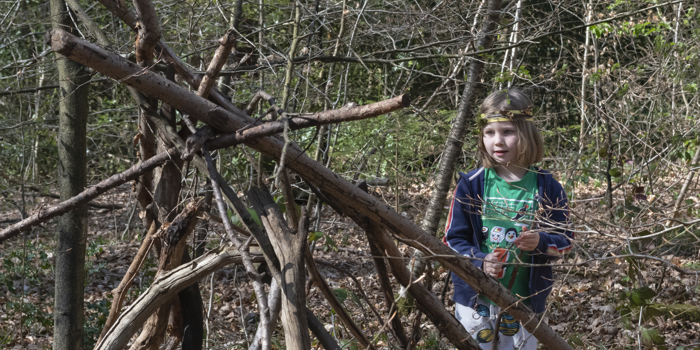 A child building a camp in the woods from sticks and fallen branches.