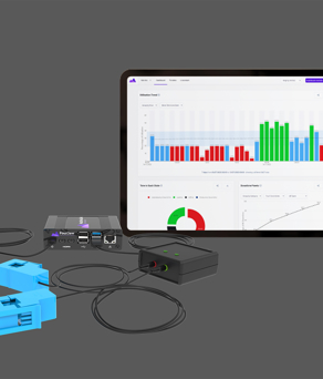 A set of electronic monitoring devices and accessories displayed on a gray surface, including blue current sensors, a black plug, a small black control box, and a central unit with multiple ports. A tablet screen in the background shows a dashboard with colourful bar charts, a pie chart, and line graphs, indicating energy or data analytics.