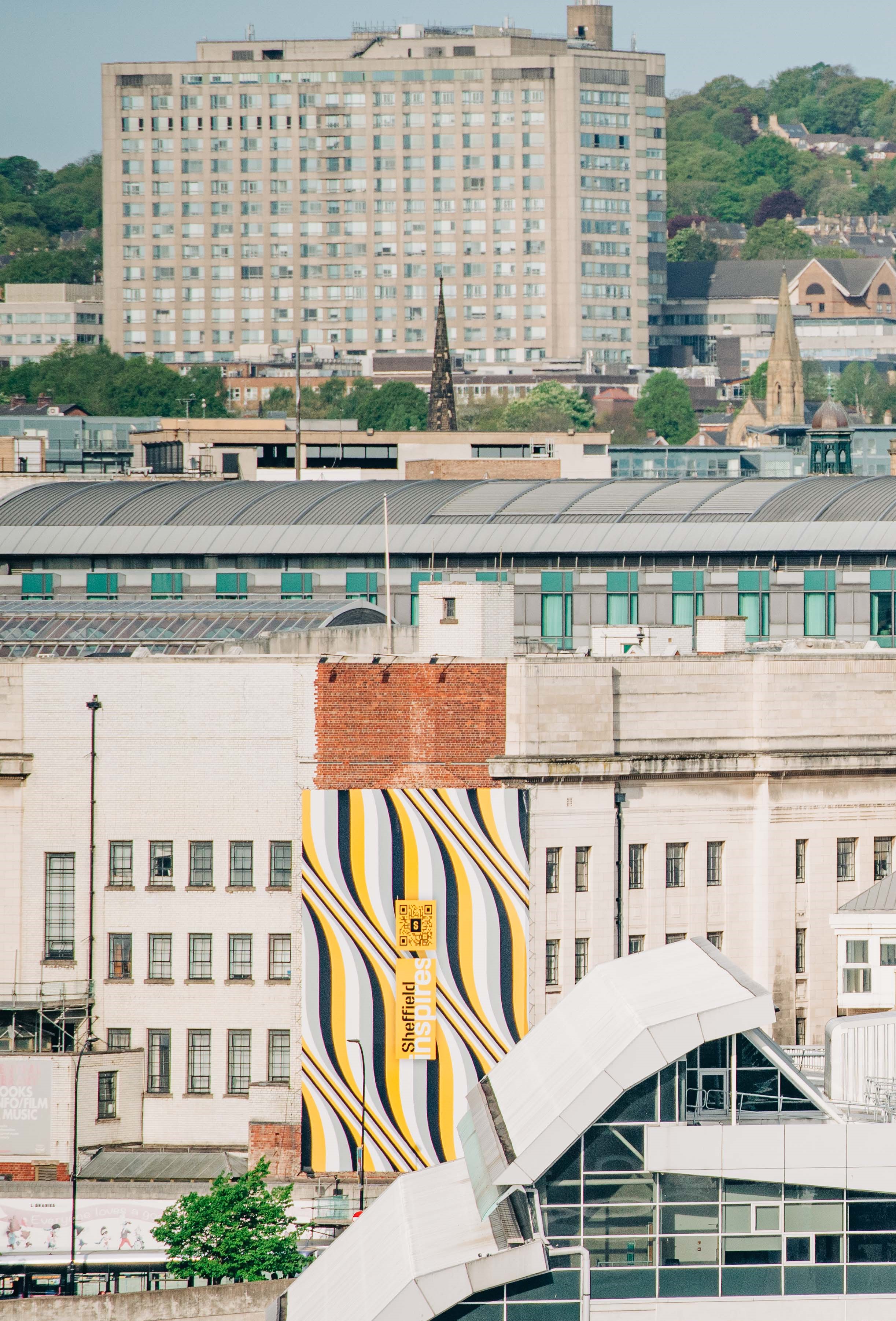 A city view with various buildings and the huge Sheffield Inspires branding shown on the side of a building in the middle of them