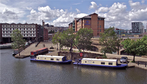 A view of Victoria Quays and the canal basin in the centre of Sheffield on a sunny day. There are several narrow boats moored up.