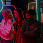 Three people at a neon-lit arcade.