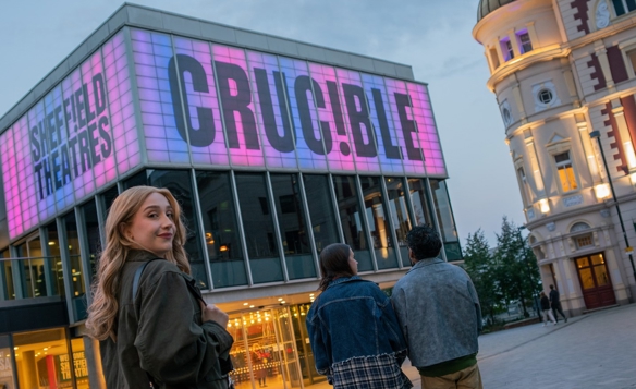 Sheffield Theatres’ Crucible building glowing pink at dusk, showing people arriving for an evening performance in the city centre.
