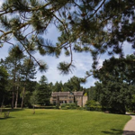 A view across a grassy area in Whirlow Brook Park, that is banked by well-tended boarders, hedges and trees, with Whirlow Brook Hall in the distance.