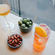 A bowl of olives, a bowl of nuts, a glass of wine and a cocktail on a table.