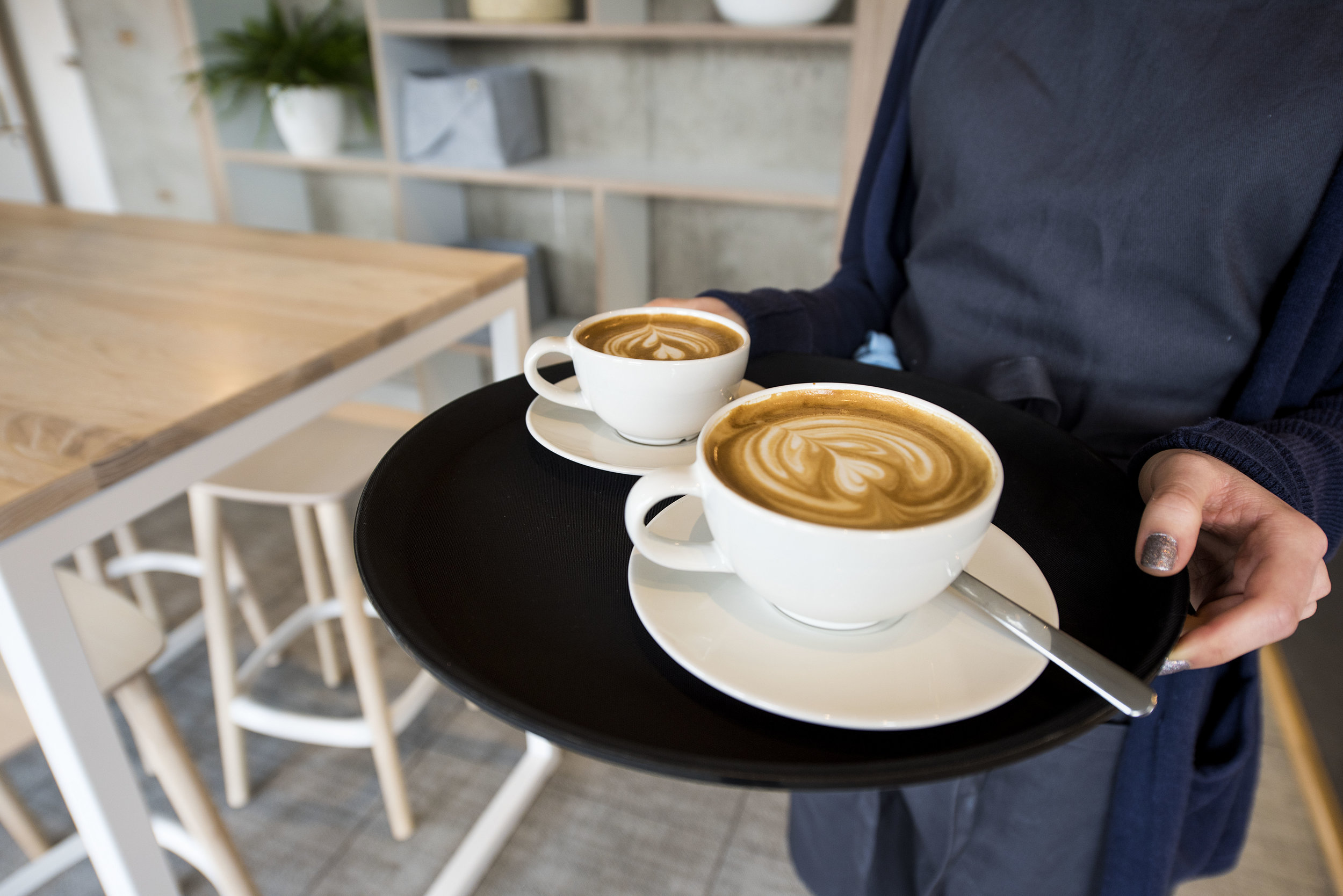 Two cappuccinos being carried on a tray.