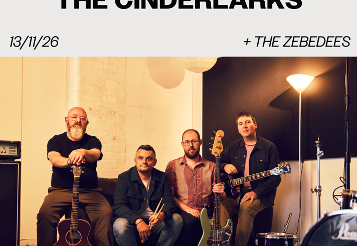 Promotional poster for a Sidney & Matilda gig. Large text reads “The Cinderlarks” with support from “The Zebedees.” Date: 13/11/26. Venue branding and website appear at the top. The main image shows four band members seated in a rehearsal or studio space surrounded by instruments, including acoustic and electric guitars, a bass guitar, drums and amplifiers. Warm indoor lighting and neutral tones create a relaxed group portrait.