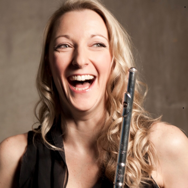 A woman, holding a flute, is smiling and laughing.