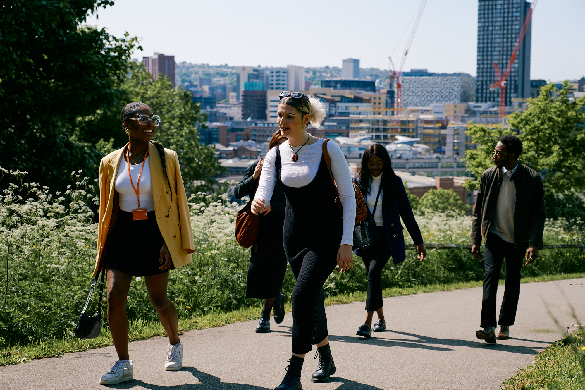 A group of people walk through a park. Behind them you can see Sheffield city centre.