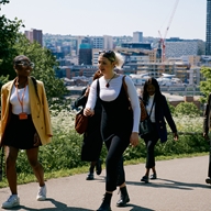 A group of people walk through a park. Behind them you can see Sheffield city centre.