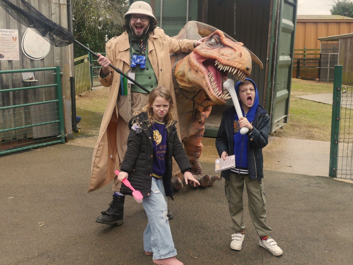 Two children and an adult pose with a large model dinosaur.