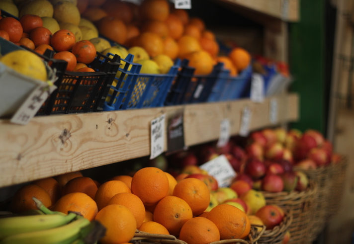 Wooden shelving with baskets full of oranges, apples, bananas and lemons.