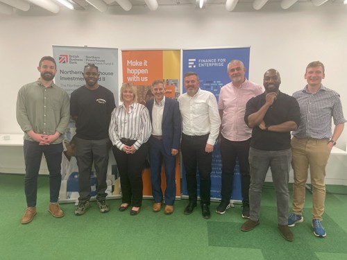 A group of eight people standing indoors in front of three vertical banners. The banners display logos and text: “Northern Powerhouse Investment Fund,” “Make it happen with us,” and “Finance for Enterprise.” The individuals are dressed in business casual attire, and the setting appears to be a professional networking or business event.