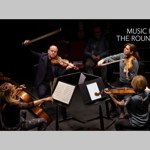 Classical musicians are sat in a circle, facing each other, performing.