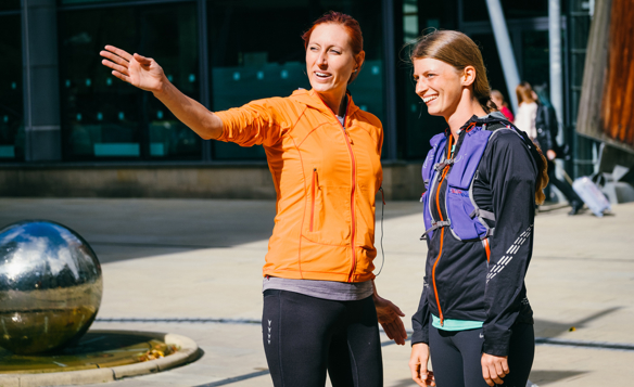 Two women in a running club, one woman is directing the other where to go.