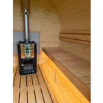 Interior of a wooden barrel-style sauna with curved timber walls and slatted bench seating along one side. A black and silver Harvia wood-burning stove stands on the left, with a metal flue extending through the ceiling. Warm sunlight highlights the natural wood grain of the walls, floor and benches, creating a clean, inviting space designed for relaxation.