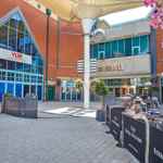 The exterior courtyard at Meadowhall featuring the Vue cinema entrance, the Oasis dining area, outdoor seating, planters and hanging baskets, with red‑brick buildings and blue‑framed windows.